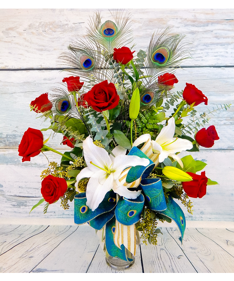 One dozen red roses with lilies and fancy greenery in an elegant, tall vase