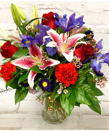 Stunning Stars, arrangement of red roses, pink lilies, purple iris and other blooms in a tall glass vase.