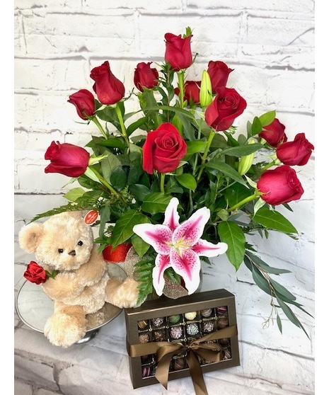 One dozen red roses with lilies and fancy greenery in an elegant, tall vase