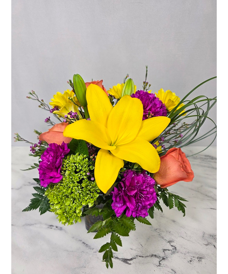 Bold, bright mix of lilies, roses, daisies, day lilies and other colorful flowers in a glass cube vase.