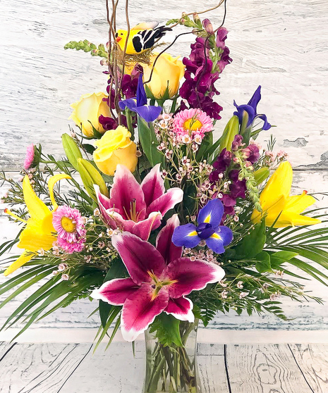 A beautiful garden style arrangement of spring colors! Stargazer lilies, iris, orchids and more are accented with ribbon, curly willow and a sweet spring bird.