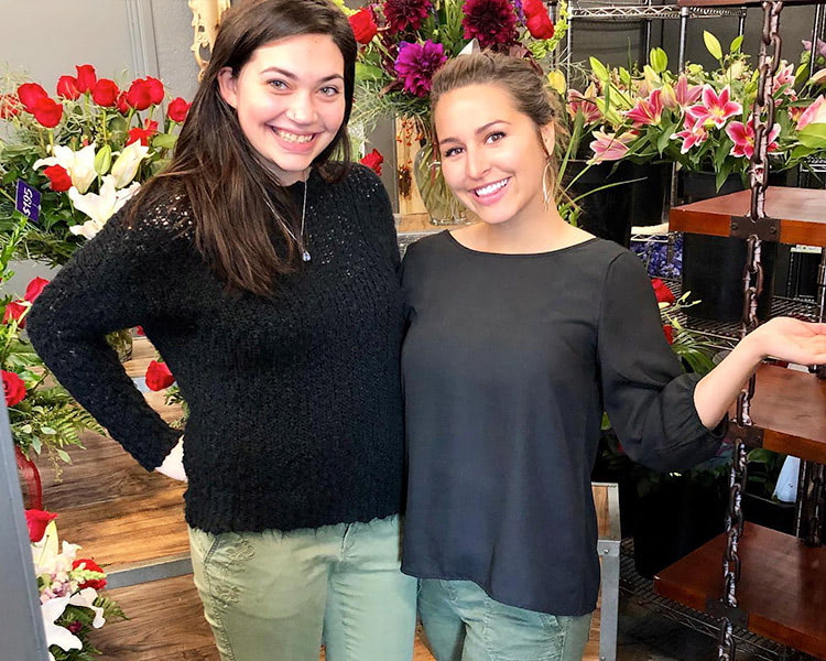 A pair of happy employees pose before dozens of beautiful bouquets
